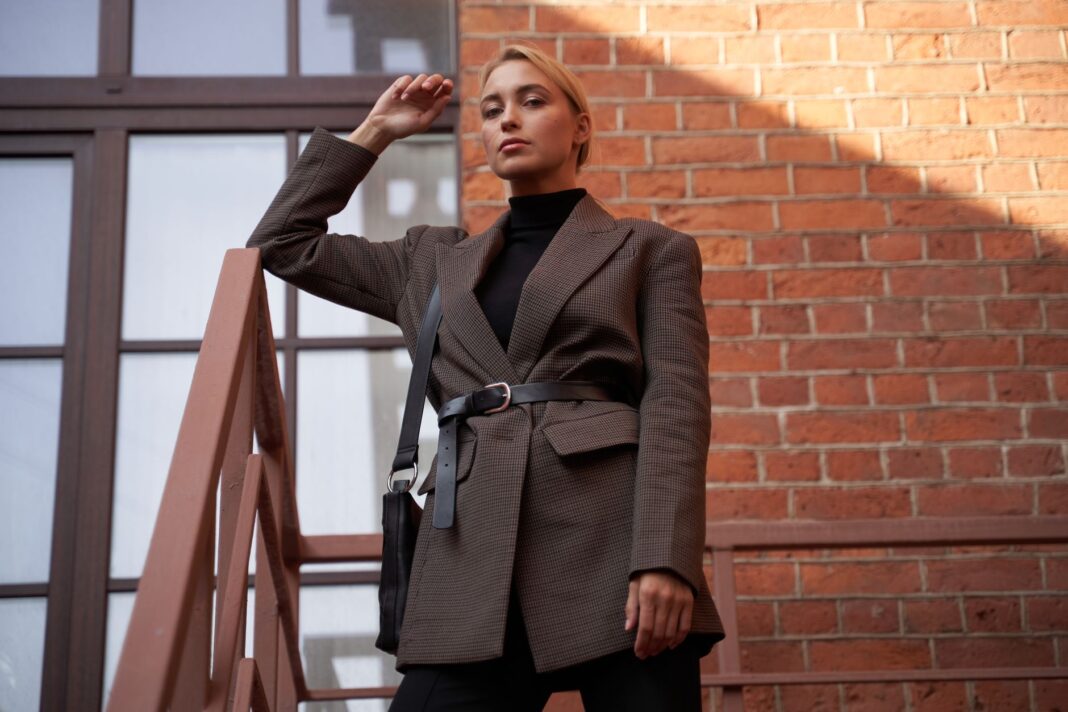 Elegancka kobieta w marynarce pozuje na schodach przy ceglanej ścianie Elegancka kobieta w marynarce pozuje na schodach przy ceglanej ścianie