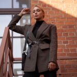 Elegancka kobieta w marynarce pozuje na schodach przy ceglanej ścianie