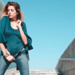 Stylowa kobieta w body i jeansach pozuje pewnie pod błękitnym niebem