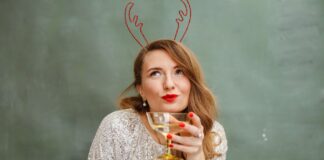 Kobieta w cekinowym topie z czerwonymi ustami trzyma drinka w pomieszczeniu